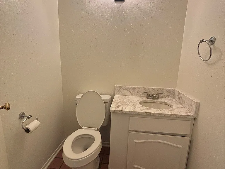 Compact powder room featuring a toilet, a single vanity with an integrated sink, a faux-marble countertop, and a white base cabinet with decorative paneling