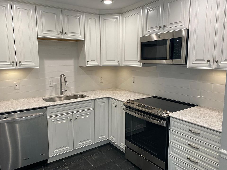 Brand new cabinets, range, microwave, countertops, under cabinet lighting, garbage disposal, and white subway tile backsplash.