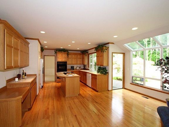 Generous sized Kitchen features abundant cabinetry, tile countertops, island with breakfast bar, and gas cooktop, pantry, built-in task desk, hardwood floors, and informal dining area with glass skywall, and French door to patio