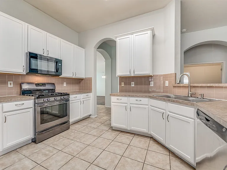 Kitchen featuring white cabinetry, tile backsplash, stainless steel appliances, and tile flooring