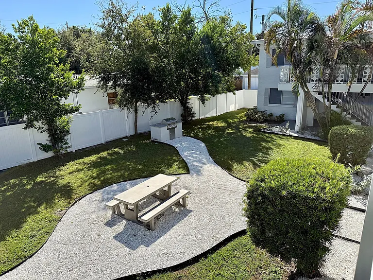 Charming backyard with a picnic table, lush greenery, and a modern BBQ grill, perfect for outdoor relaxation.