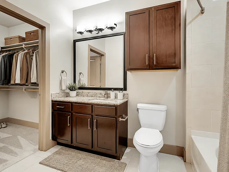 A bathroom with a white toilet, a sink with a mirror above it, and wooden cabinets.