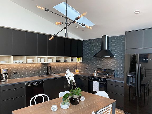 Chef's Kitchen with black stainless steel appliances, quartz countertops, tile backsplash and skylight.
