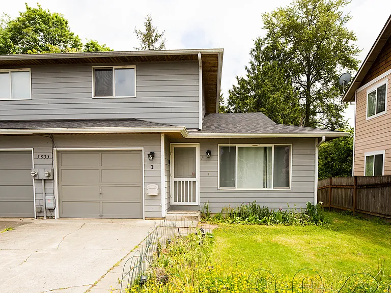 Front exterior view featuring attached garage, spacious driveway, mature landscaping, and a quiet residential setting with great curb appeal.