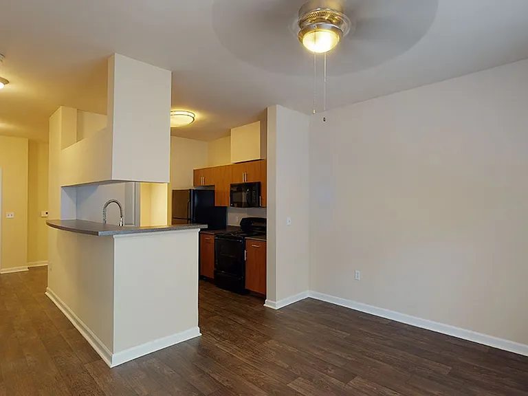 Apartment kitchen with stainless steel appliances, dining and living room with wood-style flooring.