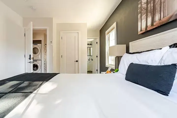 Spacious bedroom with a large bed, window for natural light, and convenient access to nearby laundry and bath areas.