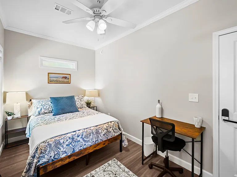 Furnished bedroom with a comfortable bed, ceiling fan, and a dedicated desk area for work or study.