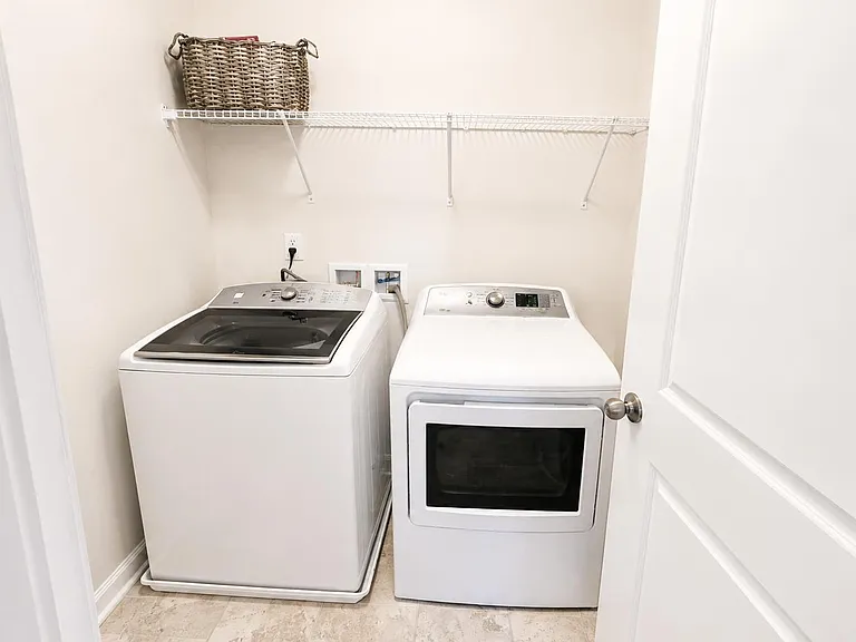 Dedicated laundry closet with full-size washer and dryer plus a wire shelf for convenient storage and organization.