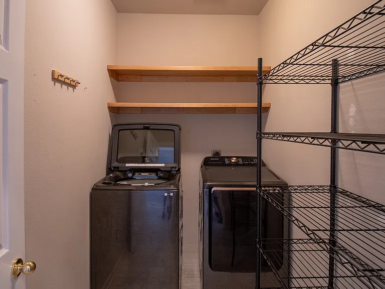 Dedicated Laundry Room: Enjoy the convenience of a separate, dedicated laundry room equipped with a modern, high-capacity washer and dryer. Built-in floating wooden shelves and a large wire storage rack provide ample space to keep your home organized.