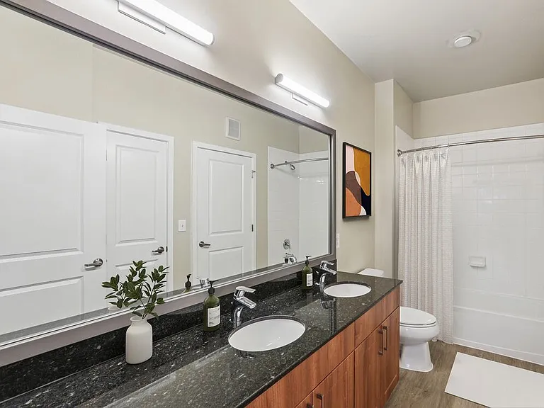 Renovated Package I bath with black granite countertop, oak cabinetry, new framed bathroom mirror, and hard surface flooring