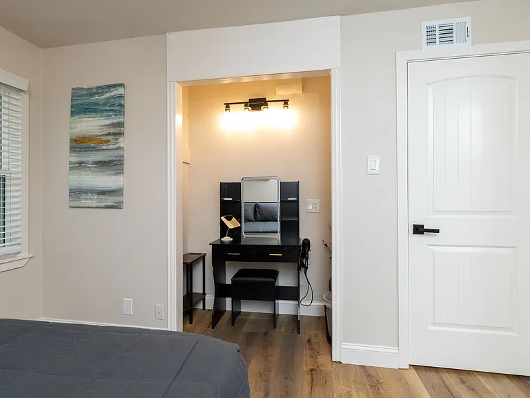 The primary bedroom includes a private vanity workspace with bright lighting, a sleek desk, shelves, and a cushioned stool_perfect for getting ready or using as a quiet, focused work area.