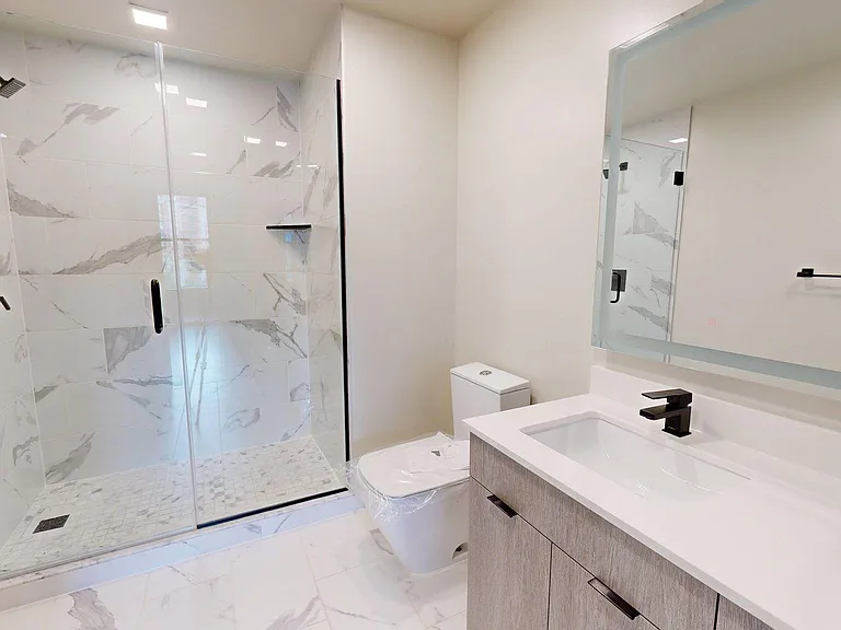 Apartment Bathroom with glass enclosed shower, LED vanity mirror and Tile Floor.