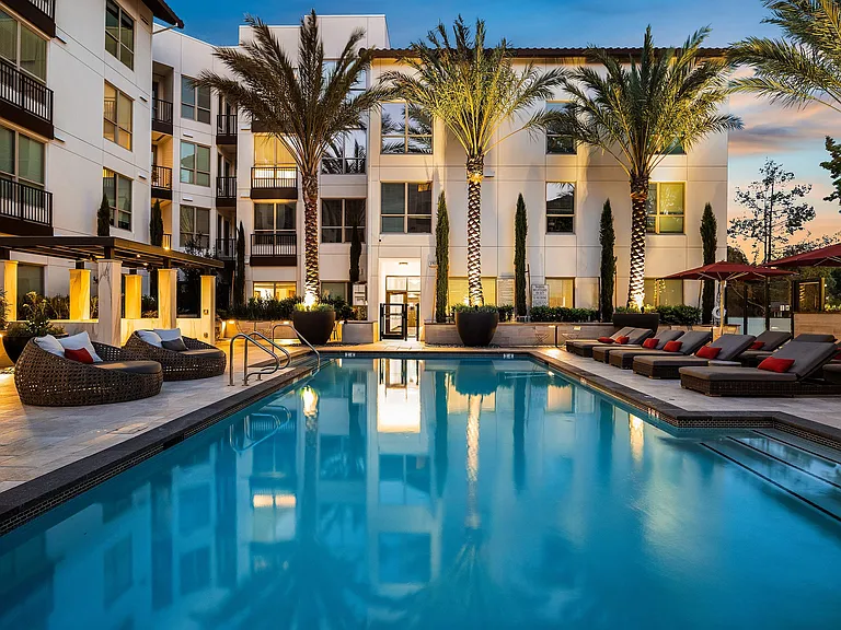 Twilight poolside with glowing water, landscaping, and seating