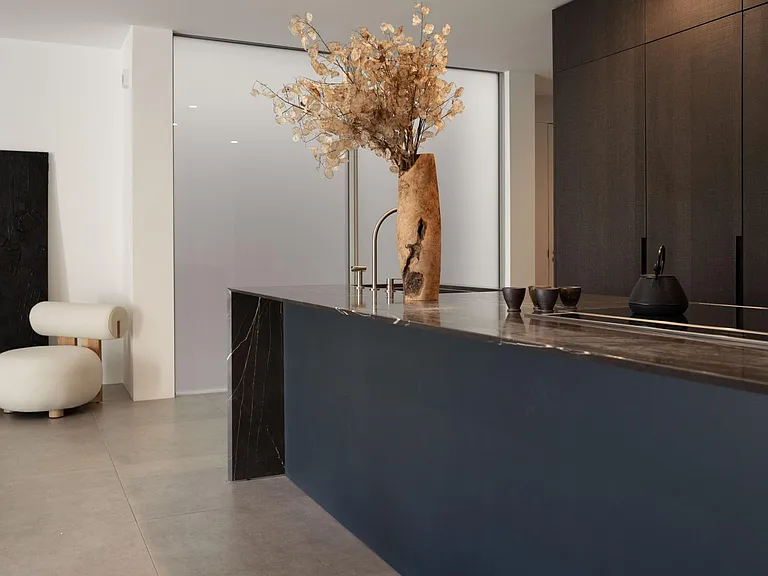 Versatile Eat-in Kitchen Island _ A sophisticated kitchen space for hosting finished in a natural marble, dark oak cabinetry, stainless steel shelving, and dramatic lighting to set the perfect mood.