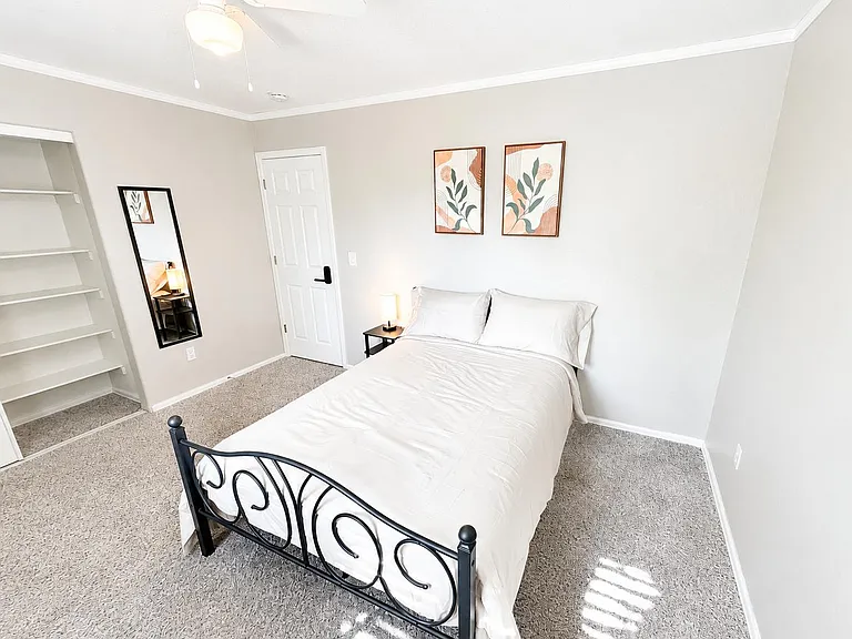 Furnished bedroom with open shelving, soft carpet, ceiling fan, and bedside table, offering comfortable space to unwind.