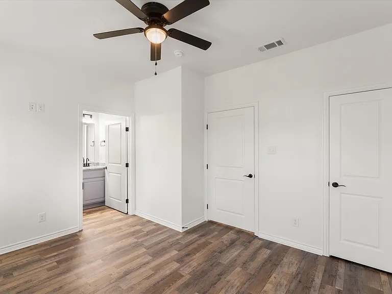 Spacious room featuring wood-finish flooring, a ceiling fan with integrated lighting, and white trim