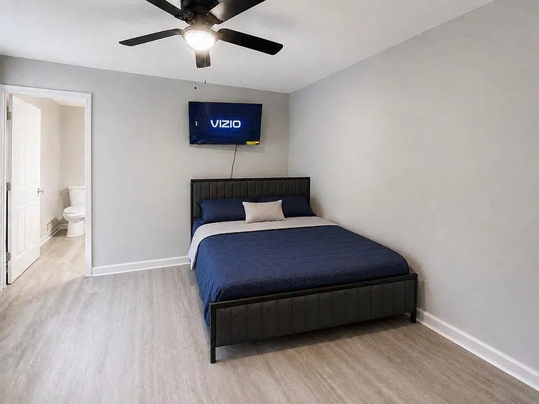 Private bedroom with queen bed, ceiling fan, wall-mounted TV, and easy access to the nearby bathroom.
