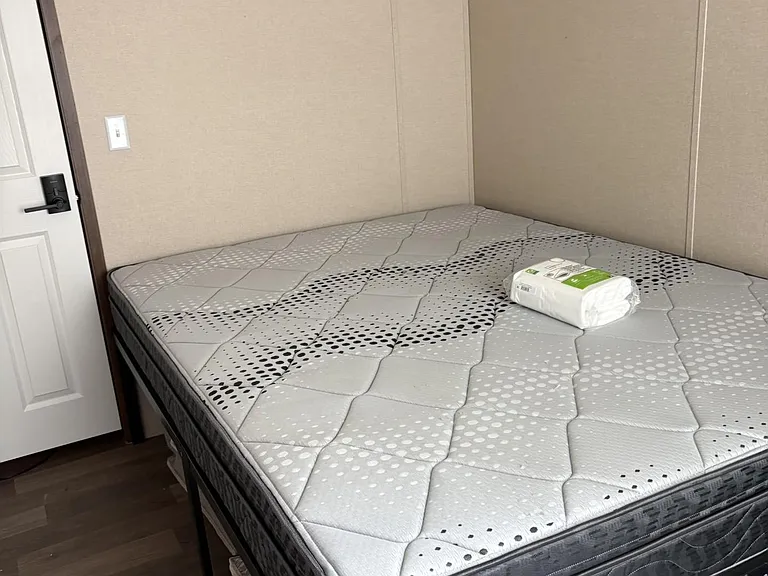 Furnished bedroom featuring a sturdy bed frame with a full mattress and easy-care flooring, set beside a private entry door.