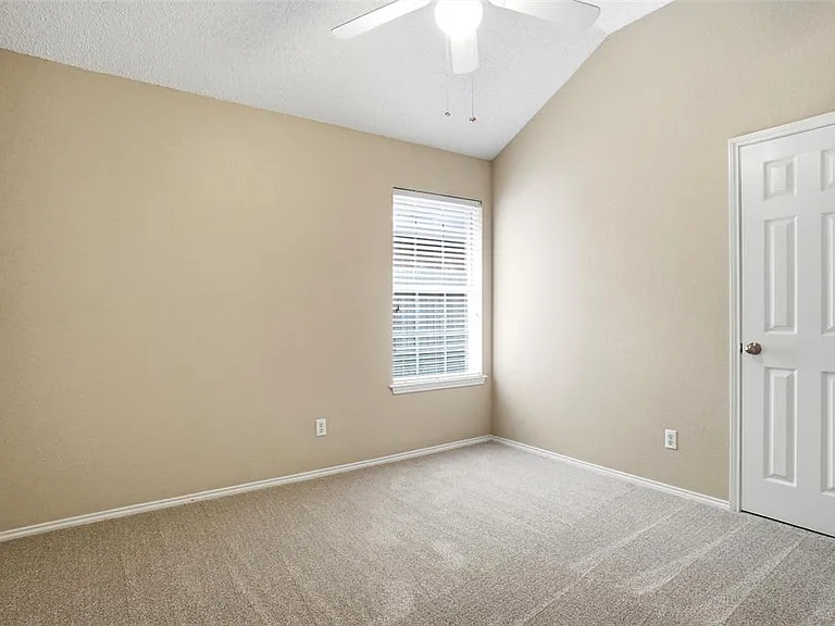 Carpeted room with a vaulted ceiling and a single window featuring horizontal blinds