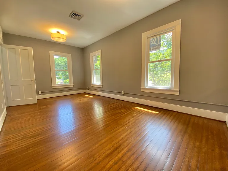 Spacious living and dining area filled with natural light, featuring brand-new energy-efficient windows and beautifully refinished original hardwood floors.
