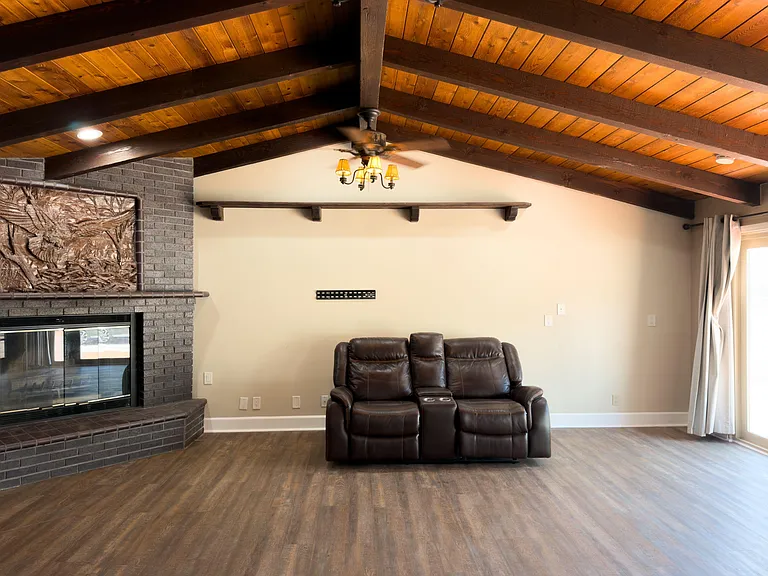 Spacious living room with vaulted wood-beam ceiling, brick fireplace, and sliding doors for easy outdoor access.