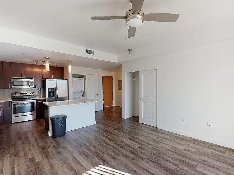 Apartment kitchen with stainless steel appliances, dining and living room with wood-style flooring.