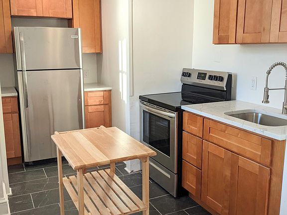 Fully renovated kitchen with stainless steel appliances, quartz countertops, solid wood cabinets, tile, and included rolling kitchen island