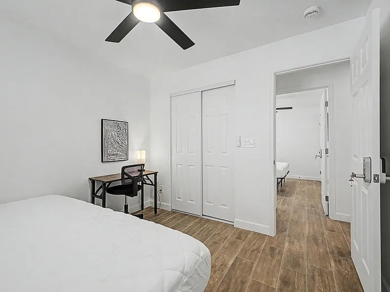 Private bedroom with wood-look flooring, ceiling fan, sliding-door closet, and a dedicated desk workspace.