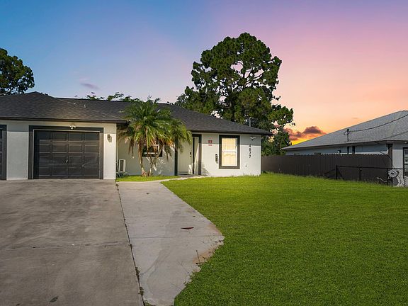 Single-story home with a wide driveway, attached garage, and a spacious front lawn with mature landscaping.