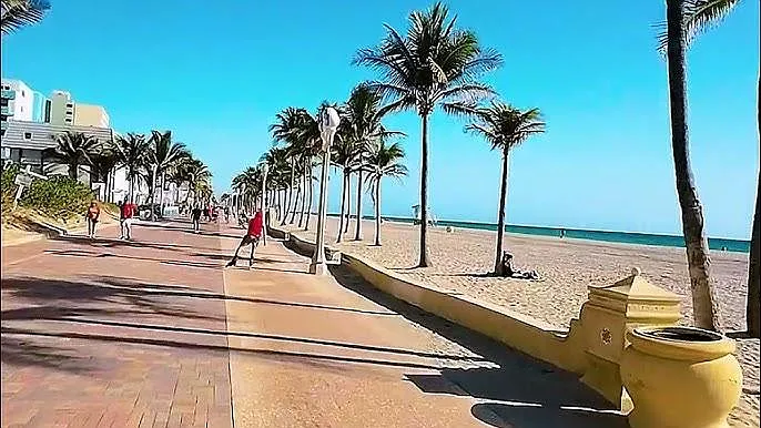 Beachfront promenade with palm-lined walkway and direct access to sandy shoreline and ocean views.