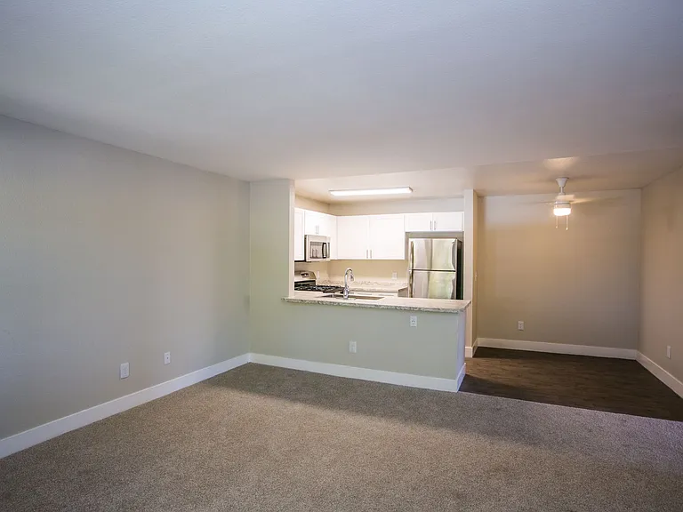 Carpeted living area with large baseboards, two-tone paint, and view of kitchen and dining area.