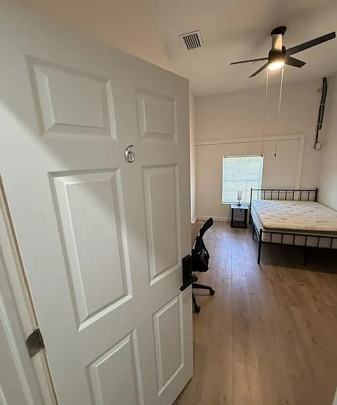 Spacious bedroom with wood-look flooring, ceiling fan, and a window for natural light, plus room for a desk and nightstand.