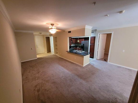 View of living room, dining area, and kitchen. Note front closet and bookshelf near the entrance. A small office area with a built-in desk and additional bookshelf is near the front door, across from the bathroom (not visible in this photo)