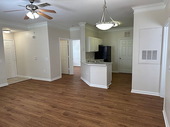 Charming open-concept living space featuring elegant wood-style floors, modern ceiling fans, and a sleek kitchen with white cabinetry and black appliances. Charming open-concept living space featuring elegant wood-style floors, modern ceiling fans, and a 
