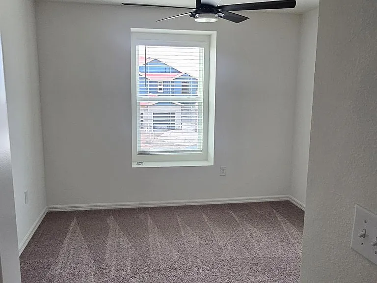 Secondary bedroom featuring carpet flooring, ceiling fan, and window providing natural light_ideal for guests, family, or a home office.