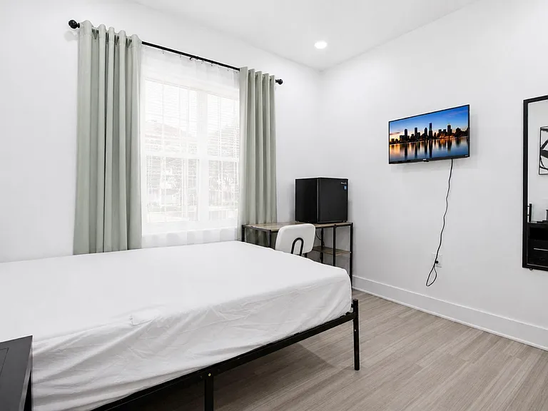 Private bedroom with a large window, bed, desk workspace, and wall-mounted TV for comfortable everyday living.