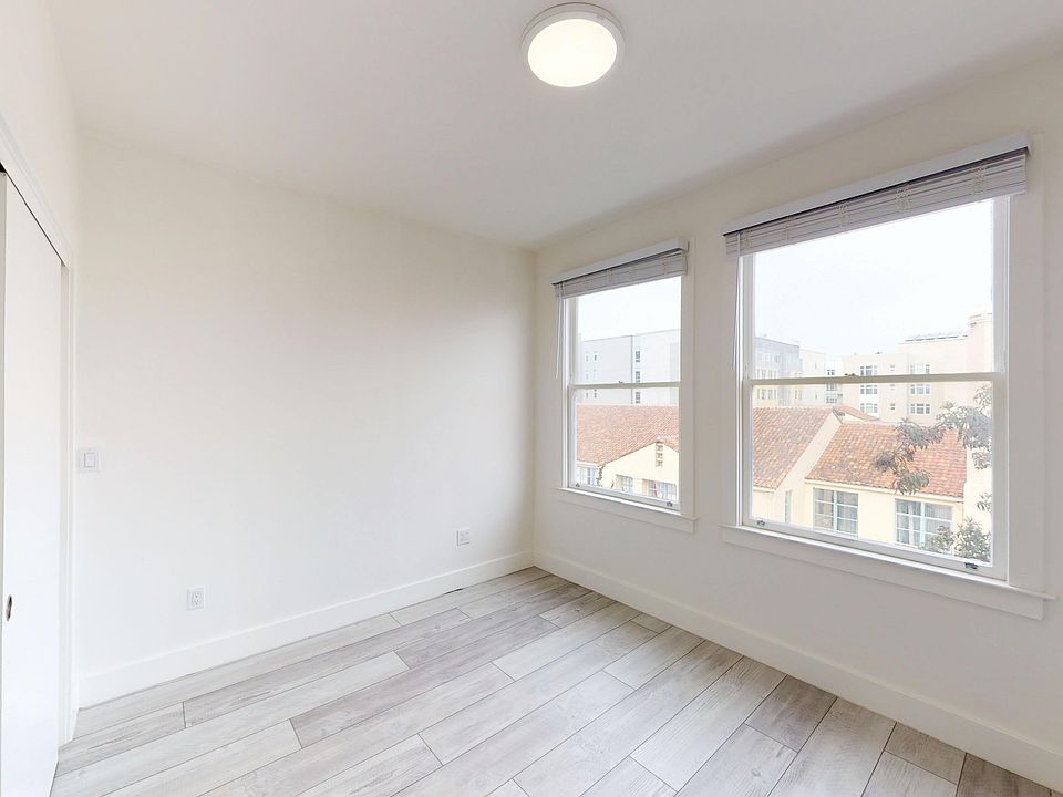 Bright, minimalistic room with two windows, and wood flooring, featuring a closet door to the left