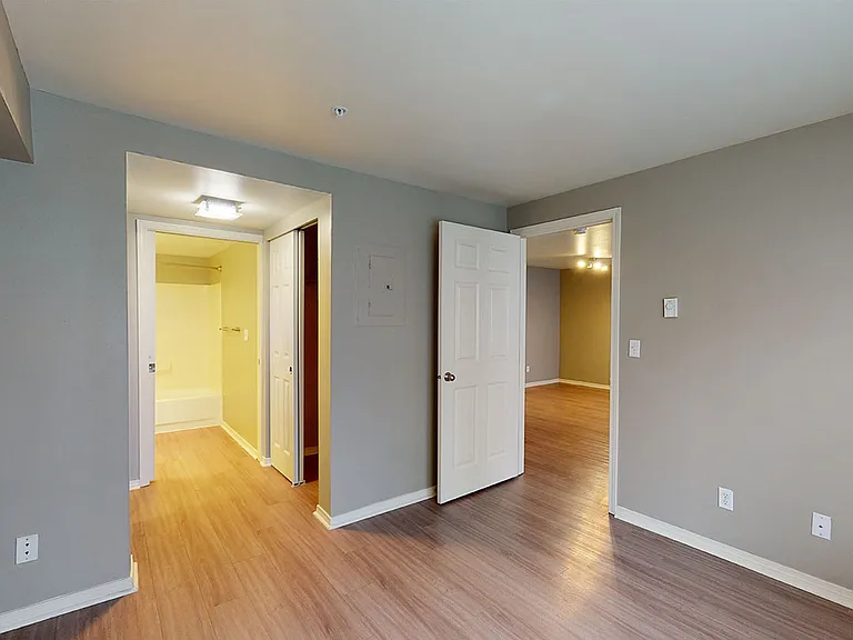 Spacious apartment bedroom with attached bathroom and wood-style flooring.