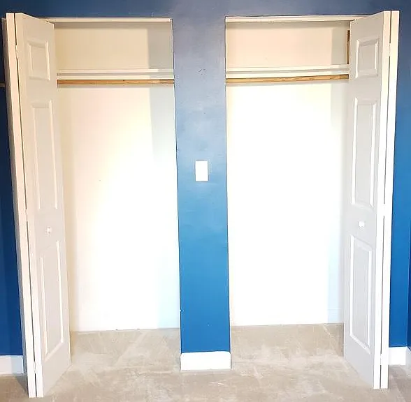 Bedroom closet doors open. One wall-to-wall closet inside with hanging rail and overhead shelf with 3+ ft of vertical space (extending behind the top of the blue wall).