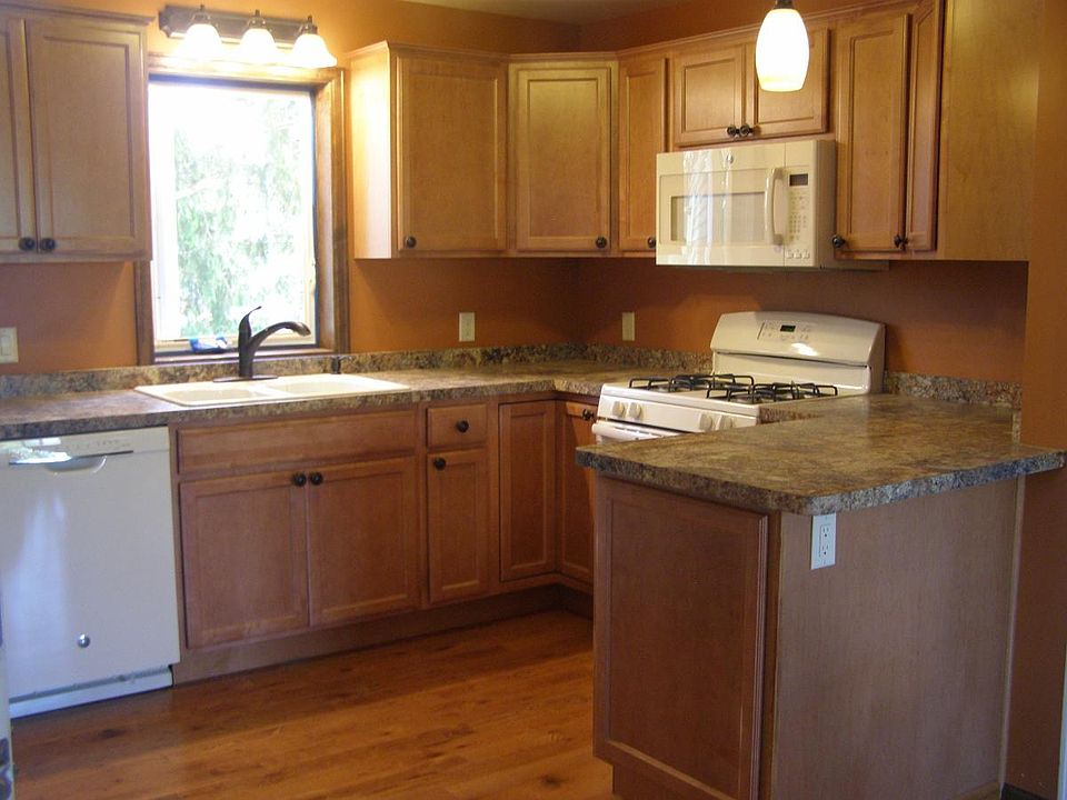 Open concept kitchen. Faucet pictured has been replaced with similar Pfister brand. To the rear (not pictured) of the pennisula is the coat closet. View from window is a large mature white pine.