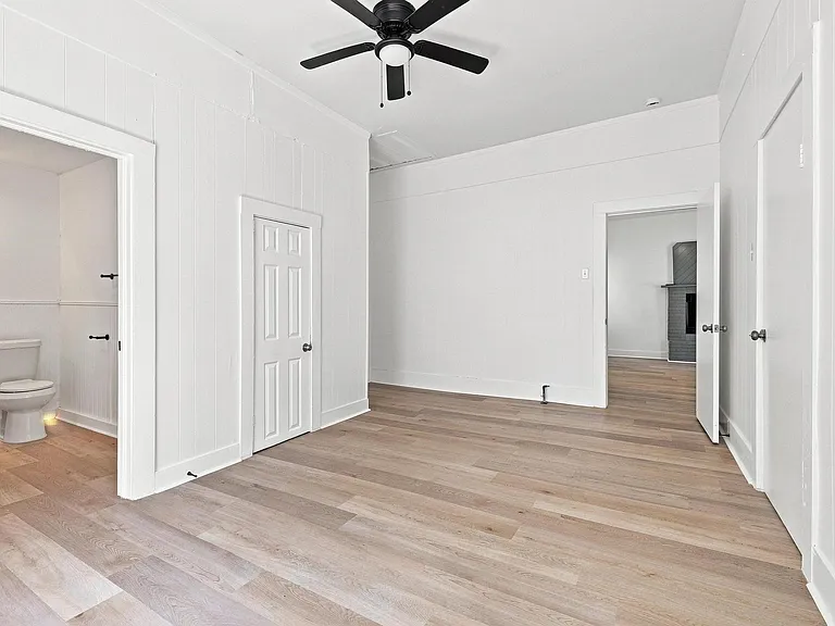Spacious room featuring light wood-finish flooring, a ceiling fan, and crisp white walls