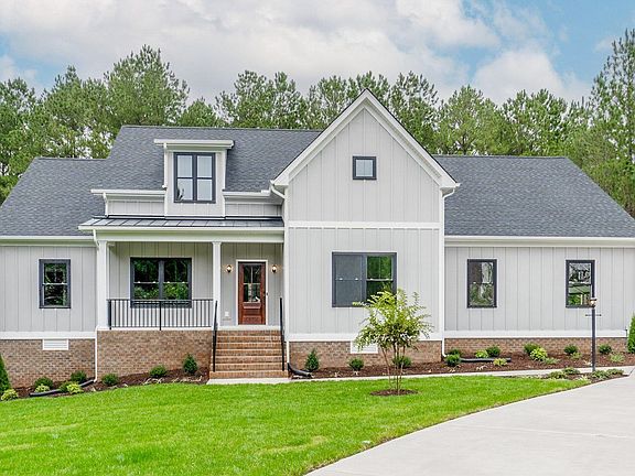 A white, modern farmhouse-style house with a gray roof and front porch, surrounded by a green lawn a