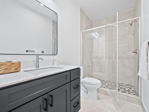 Stylish bathroom with a large vanity, expansive mirror, and a glass-enclosed tile shower with updated fixtures.