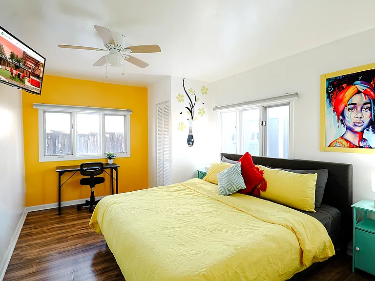 A bedroom with a refreshing mix of yellow and white walls, enhanced with a TV and a ceiling fan, combining visual warmth with airy circulation for a comfortable retreat.