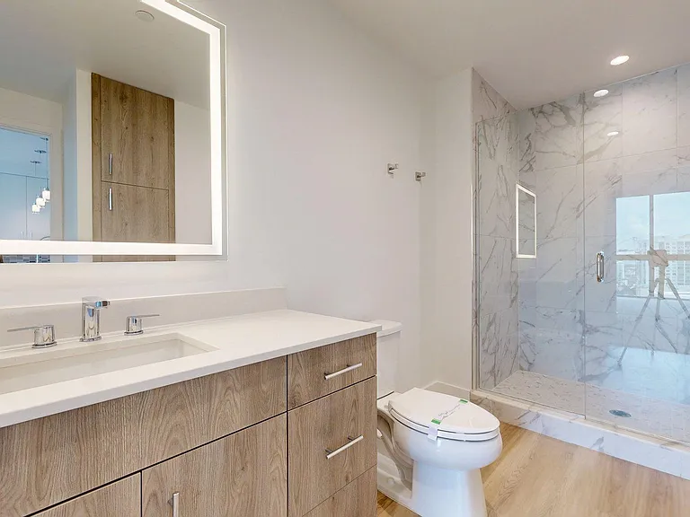 Apartment bathroom with glass enclosed shower, LED vanity mirror and wood-style flooring