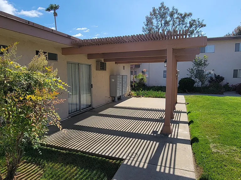 Patio with pergola and mailboxes in grassy courtyard at Plaza Verde Apartments in Escondido, California.