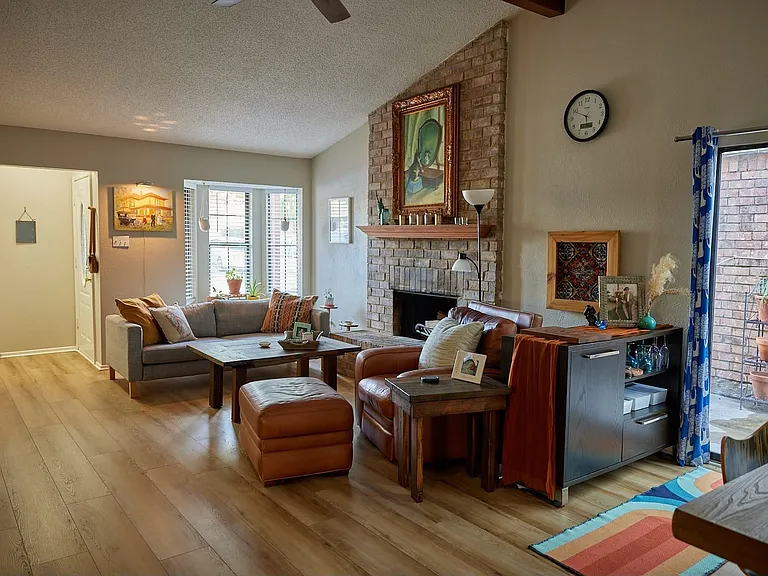 Living area with light wood finished floors, a fireplace, lofted ceiling, a ceiling fan, and a textured ceiling
