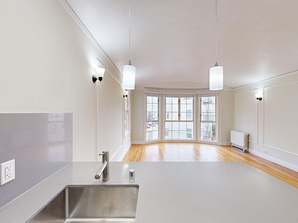Living area with large windows, wood-like floors, and a kitchen sink