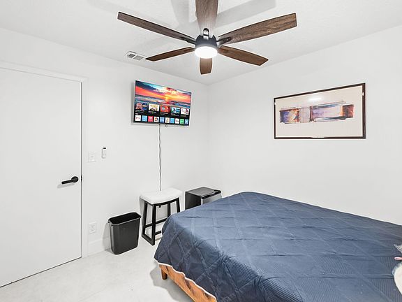 Private bedroom with ceiling fan, wall-mounted TV, and space for a full/queen bed plus a small seating or work area.