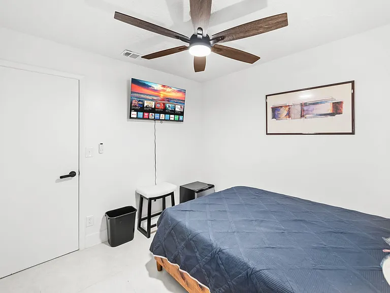 Private bedroom with ceiling fan, wall-mounted TV, and space for a full/queen bed plus a small seating or work area.